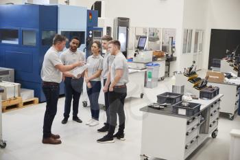 Engineering Team Meeting On Factory Floor Of Busy Workshop