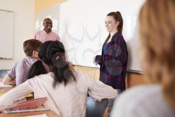 Female High School Pupil Writing On Whiteboard In Class