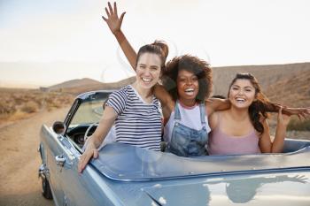 Portrait Of Three Female Friends Enjoying Road Trip In Open Top Classic Car
