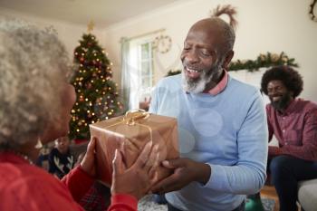 Senior Couple Exchanging Gifts As They Celebrate Christmas At Home With Family