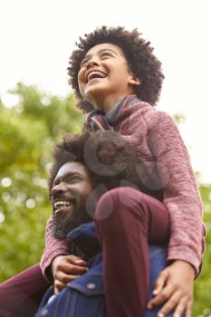 Black middle aged man carrying his son on his shoulders in the park, close up, low angle