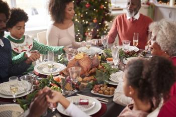 Multi generation mixed race family sitting at Christmas dinner table holding hands and saying grace, elevated view