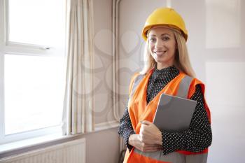 Portrait Of Female Surveyor In Hard Hat And High Visibility Jacket With Digital Tablet Carrying Out House Inspection