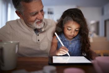 Senior Hispanic man with his young granddaughter using stylus and tablet computer, front, close up