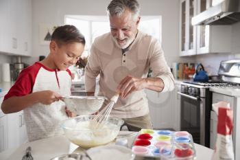 Pre-teen boy making cake mixture in the kitchen with his grandfather, close up