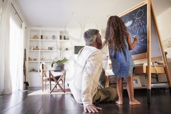 Grandfather sitting on the floor drawing on a blackboard with his young granddaughter, low angle