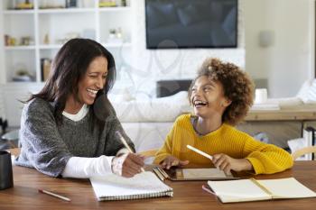 Middle aged mixed race woman sitting at a table in the dining room doing homework with her granddaughter, both laughing, close up
