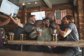 Group Of Friends Watching Game On Screen In Sports Bar