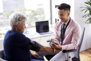 Male Doctor In Office Checking Senior Female Patients Blood Pressure