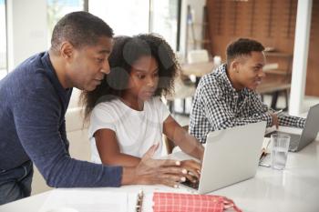 Middle aged black man helping his teenage children do their homework using laptop computers