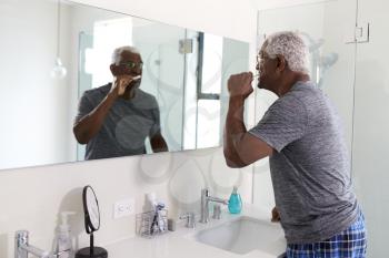 Senior Man Looking At Reflection In Bathroom Mirror Wearing Pajamas Brushing Teeth