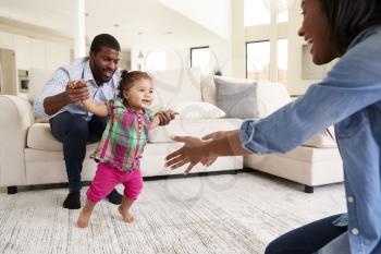 Family At Home Encouraging Baby Daughter To Take First Steps