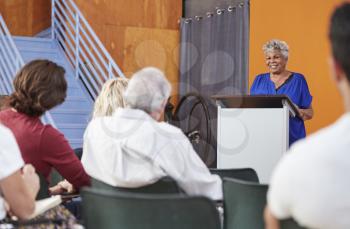 Senior Woman At Podium Chairing Neighborhood Meeting In Community Centre