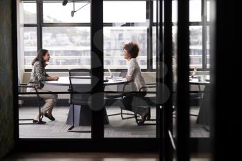 Two millennial businesswomen meeting for a job interview, full length, seen through glass wall