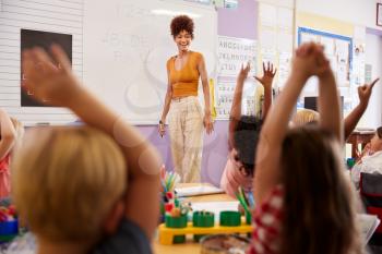 Pupils Raising Hands To Answer Question In Elementary School Maths Lesson