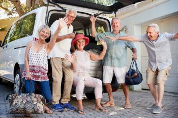 Portrait Of Excited Senior Friends Loading Luggage Into Trunk Of Car About To Leave For Vacation