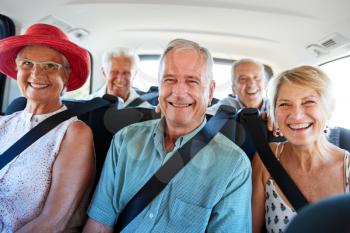 Portrait Of Senior Friends Sitting In Back Of Van Being Driven To Vacation