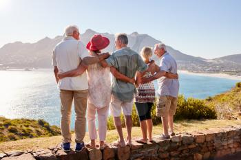 Rear View Of Senior Friends Visiting Tourist Landmark On Group Vacation Standing On Wall