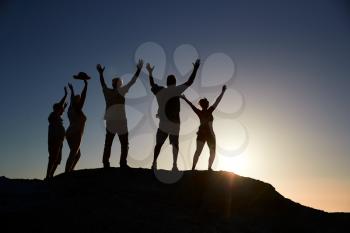 Silhouette Of Senior Friends Standing On Rocks By Sea On Vacation At Sunset With Arms Outstretched
