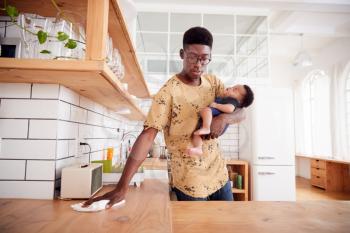 Multi-Tasking Father Holds Sleeping Baby Son And Cleans In Kitchen