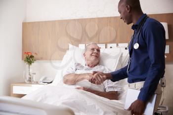 Doctor Shaking Hands With Senior Male Patient In Hospital Bed In Geriatric Unit