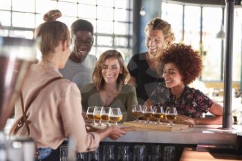 Waitress Serving Group Of Friends Beer Tasting In Bar