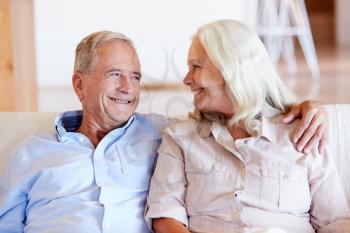 Senior white couple relaxing at home, looking at each other smiling, front view, close up