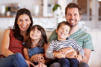 Mid adult white couple and their two young children sitting on a sofa at home smiling to camera