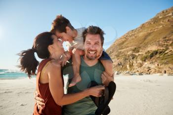 Mid adult white couple standing on a beach, dad carrying son on his shoulders, front view, close up