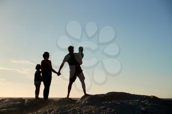 Mid adult parents and two pre-teen children standing on beach admiring view, full length, silhouette