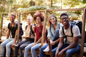 Five young adult friends on a hike sitting together smiling to camera during a break, close up