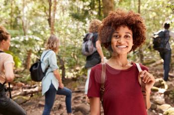 Smiling millennial African American woman hiking in a forest with friends, waist up, close up