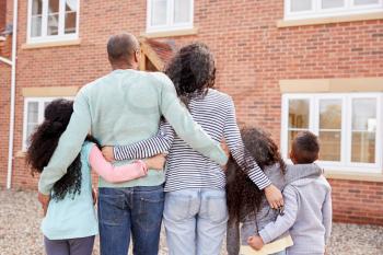 Rear View Of Family Standing Outside New Home On Moving Day Looking At House