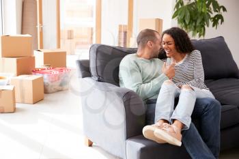 Couple Taking A Break And Sitting On Sofa Celebrating Moving Into New Home With Champagne
