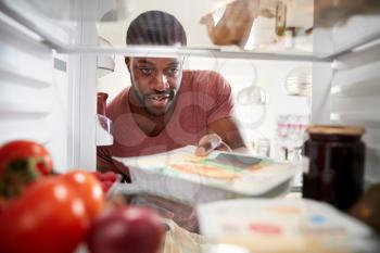 View Looking Out From Inside Of Refrigerator As Man Opens Door And Unpacks Shopping Bag Of Food
