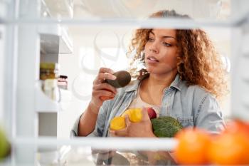 View Looking Out From Inside Of Refrigerator As Woman Opens Door And Packs Food Onto Shelves