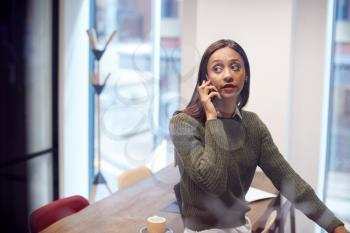 Businesswoman Sitting On Desk In Meeting Room Talking On Mobile Phone