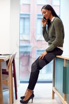 Businesswoman Sitting On Desk In Meeting Room Talking On Mobile Phone