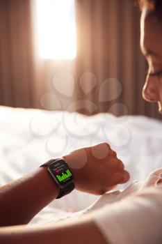 Woman Sitting Up In Bed Looking At Screen Of Smart Watch