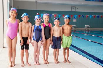 Portrait Of Children Standing On Edge Of Pool Waiting For Swimming Lesson