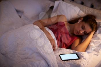 Woman Sleeping In Bed Wearing Wireless Earphones Connected To Mobile Phone