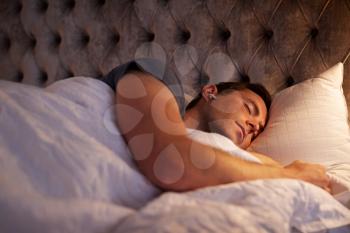Man Sleeping In Bed Wearing Wireless Earphones Connected To Mobile Phone
