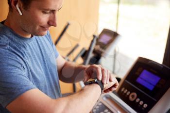 Man Exercising On Treadmill At Home Wearing Wireless Earphones Checking Smart Watch