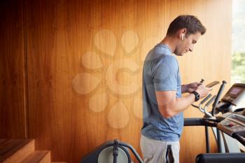 Man Exercising On Treadmill At Home Wearing Wireless Earphones Checking Mobile Phone