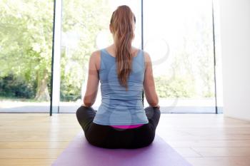 Rear View Of Young Woman Doing Yoga On Wooden Floored Studio At Home