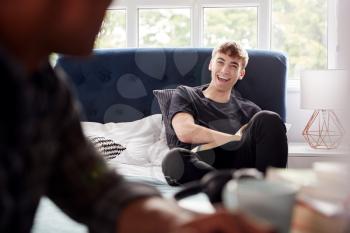 Two Male College Students In Shared House Bedroom Studying And Talking Together