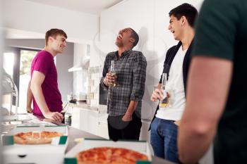 Group Of Male College Students In Shared House Kitchen Drinking Beer And Eating Pizza Together