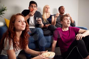 Group Of College Students In Shared House Watching TV And Eating Popcorn