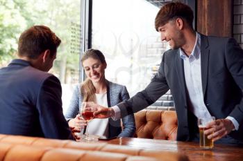 Businessman Buying Round Of Drinks For Colleagues Meeting And Socializing In Bar After Work