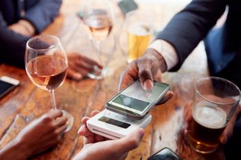 Close Up Of Businessman Paying For Round Of Drinks In Bar Using Contactless App On Mobile Phone